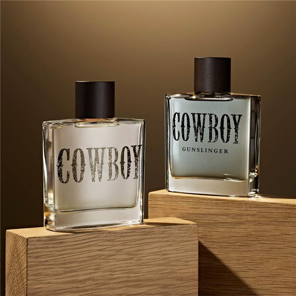 Two bottles of 'Cowboy' perfume on wooden stands with a brown background