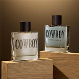 Two bottles of 'Cowboy' perfume on wooden stands with a brown background