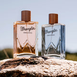 Two bottles of Wrangler Original perfume on a rock with a blurred natural background