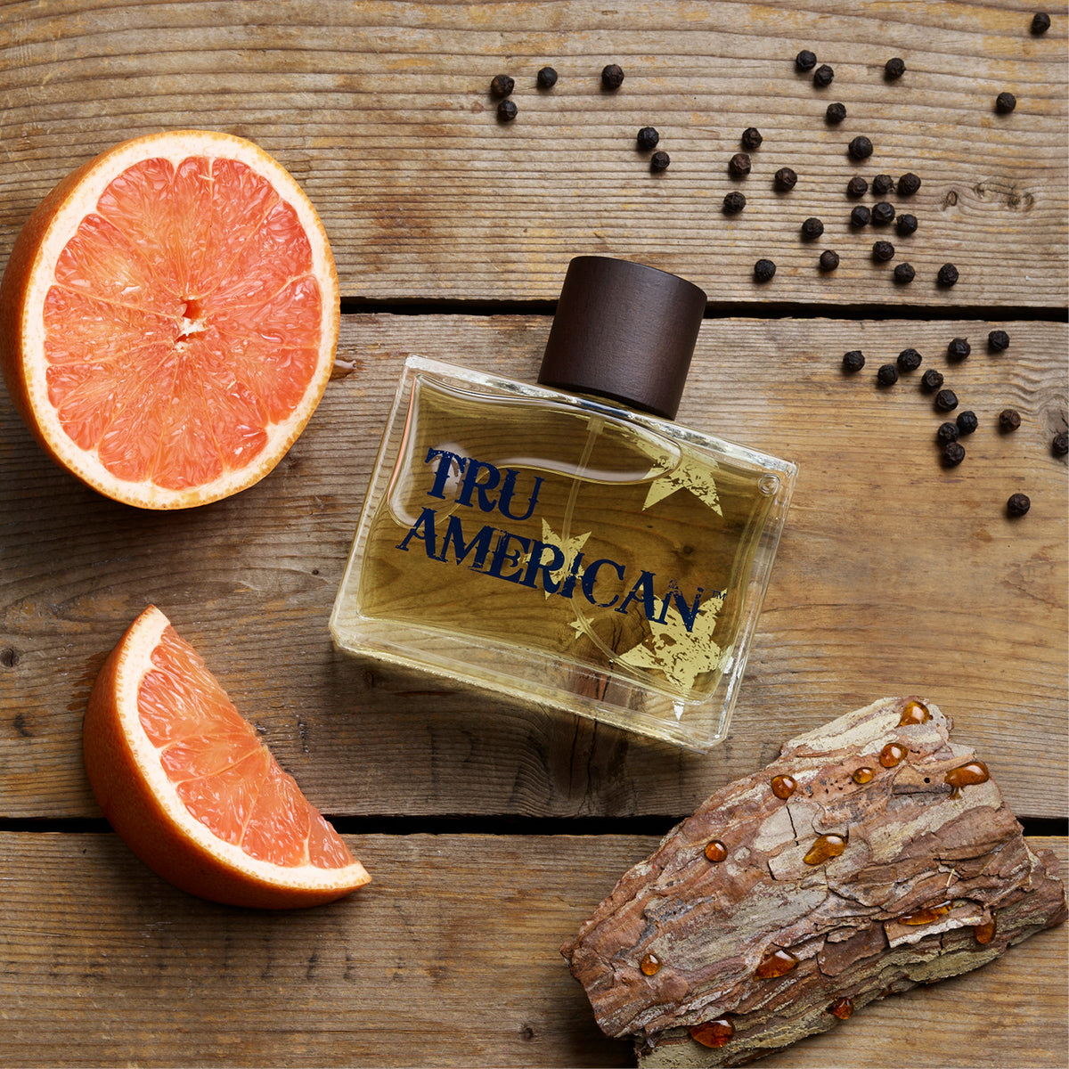 TRU AMERICAN perfume bottle on a wooden surface with grapefruit and peppercorns