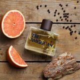 TRU AMERICAN perfume bottle on a wooden surface with grapefruit and peppercorns